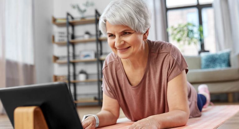 Eine lächelnde ältere Frau mit Tablet-PC-Computer beim Training auf einer Matte zu Hause