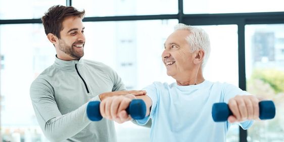 Mann trainiert mit Hanteln unter Anleitung eines Trainers