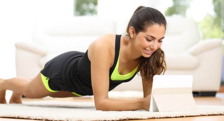Eine junge Frau macht Übungen zu Hause und folgt dabei den Anweisungen auf ihrem Tablet