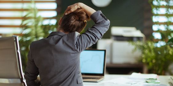 Blick von hinten auf eine moderne Geschäftsfrau in einem grauen Businessanzug in einem modernen grünen Büro, die sich streckt.